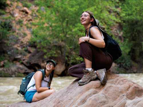 A female student sits on a large rock and looks upwards with a smile on her face